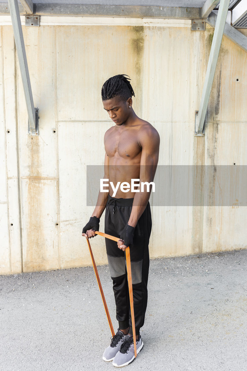 Shirtless young man exercising with resistance band outdoors