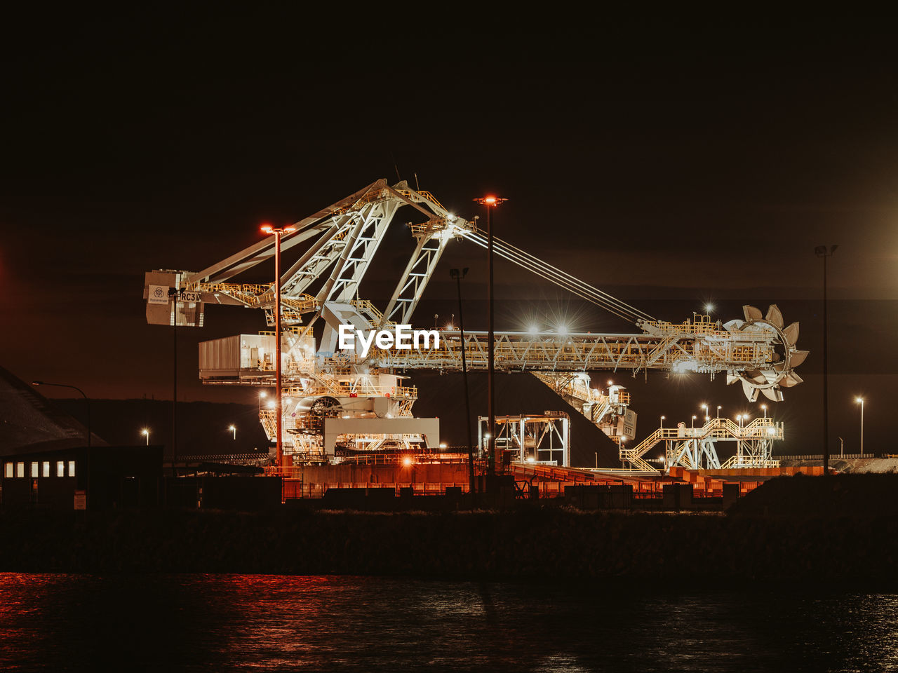 Illuminated pier by river against sky at night