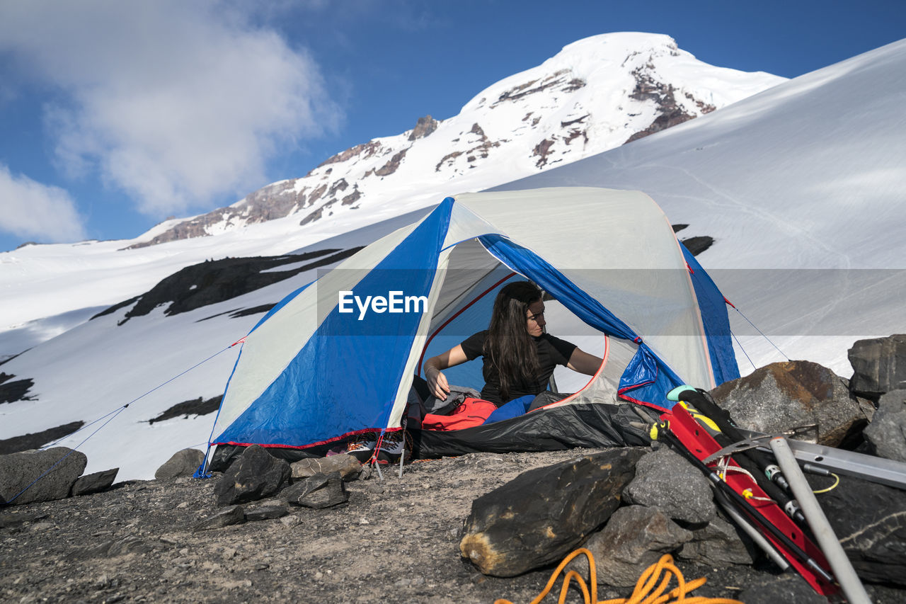 A woman reaches for something while she sits in her tent at base camp, mt. baker