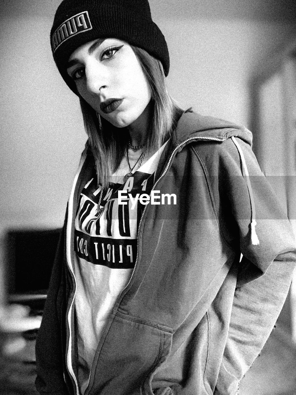 PORTRAIT OF YOUNG WOMAN WEARING HAT STANDING AGAINST WALL