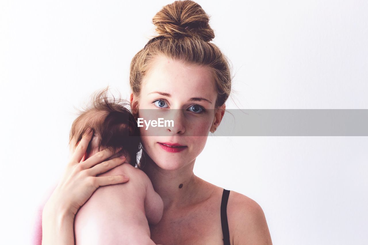 Portrait of mother carrying shirtless daughter against white background