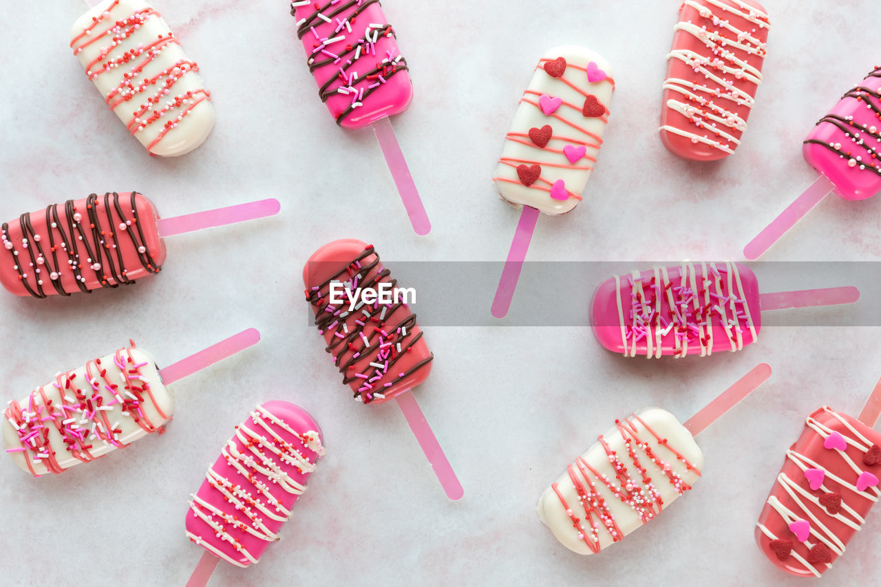 Various valentine decorated cakesicles on a pink marble surface