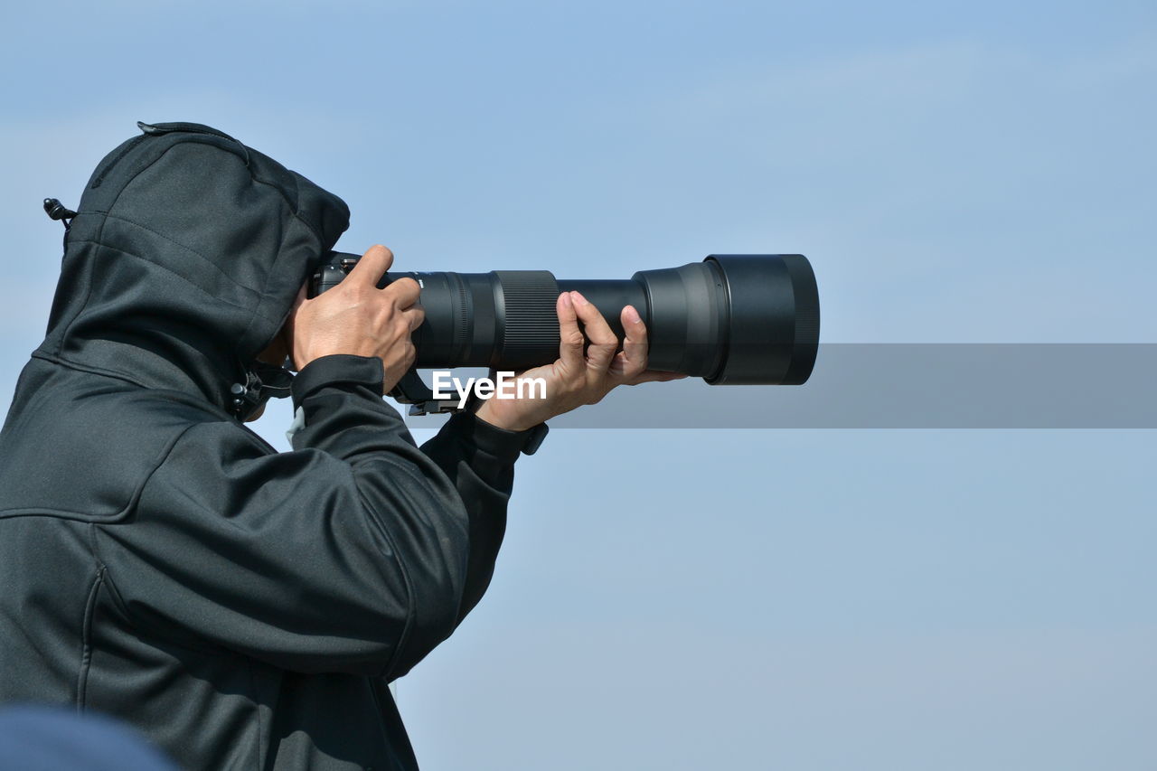 Man photographing through camera against sky