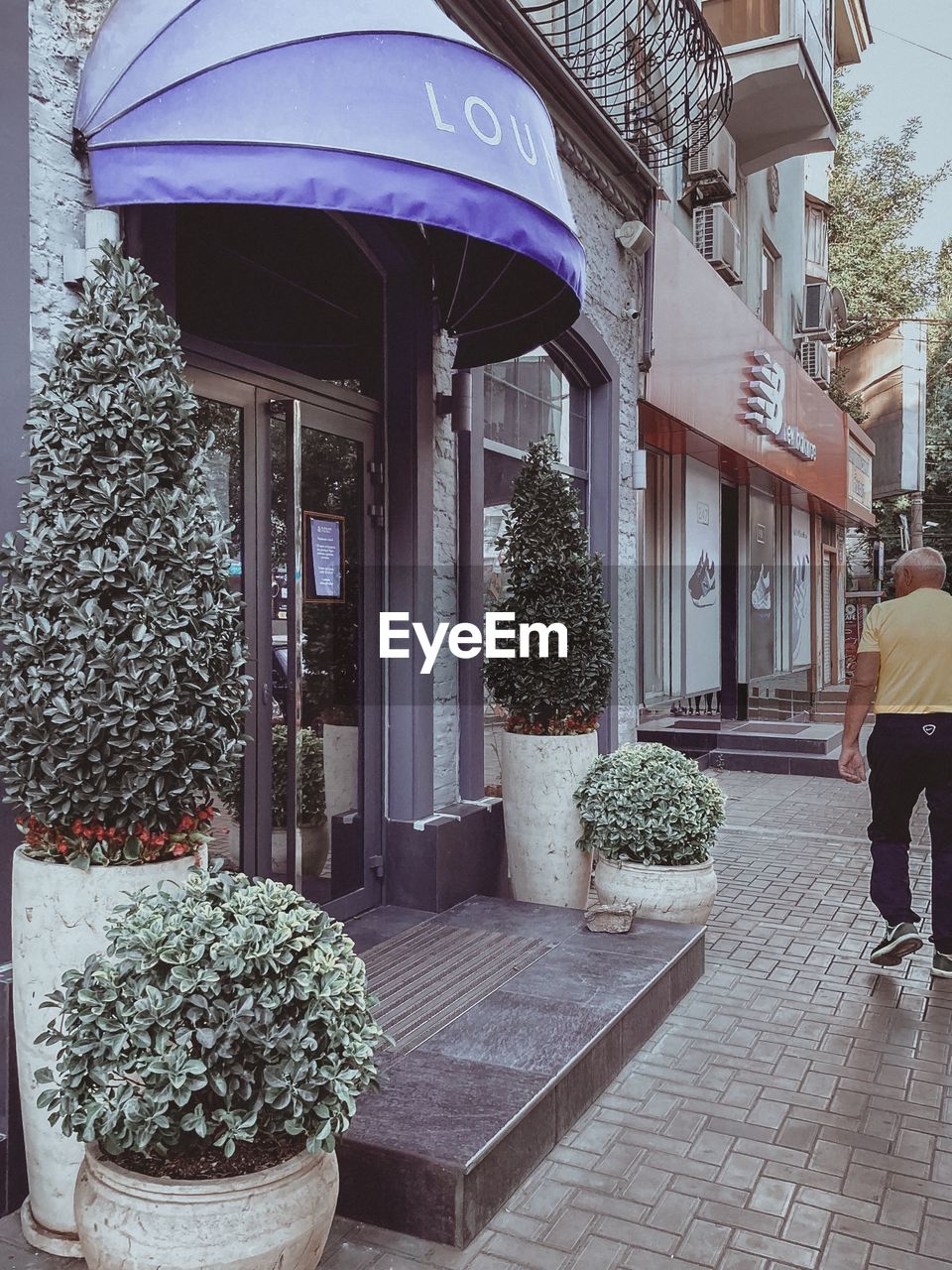 REAR VIEW OF WOMAN WALKING ON FOOTPATH AMIDST BUILDINGS