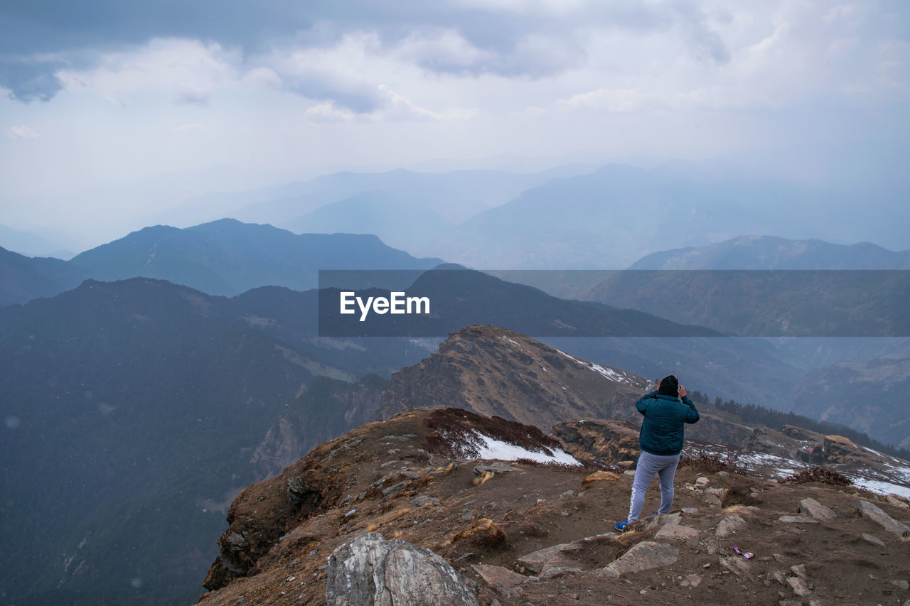 Rear view of man standing on mountain against sky