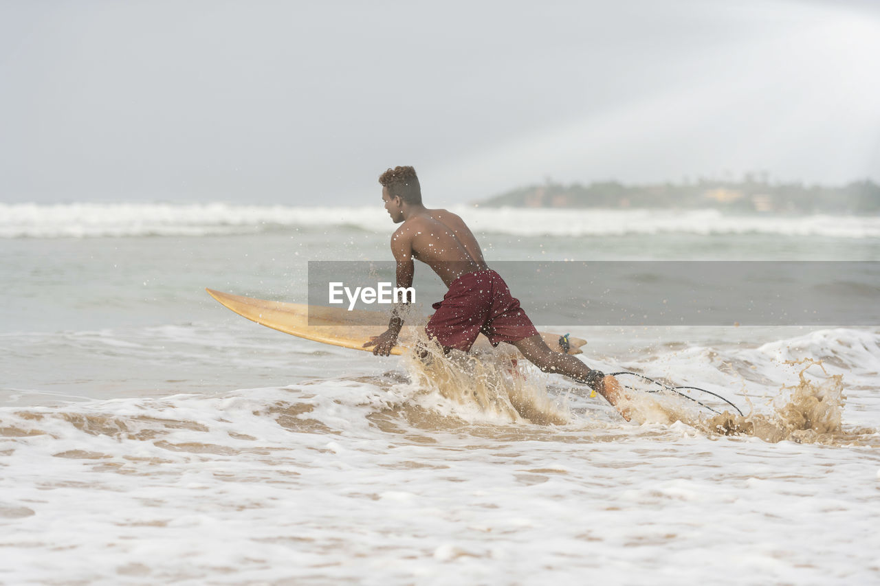 Shirtless man surfing in sea against sky