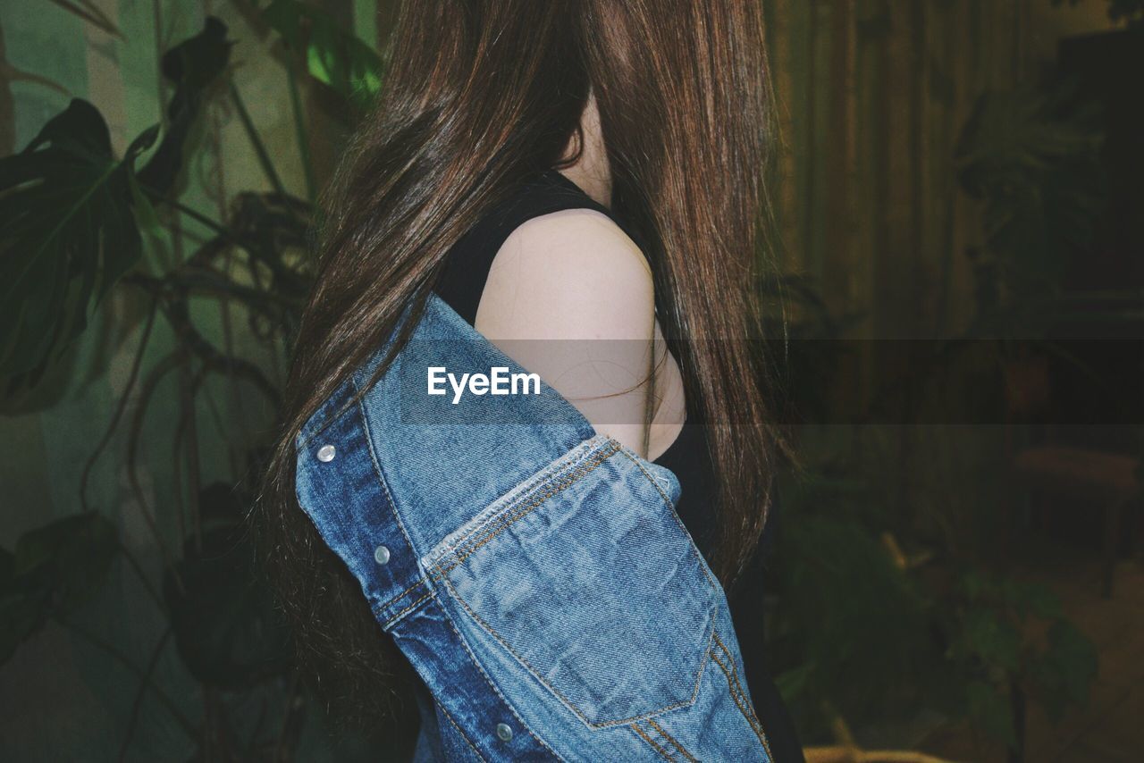 Side view of woman wearing denim jacket while standing against plants