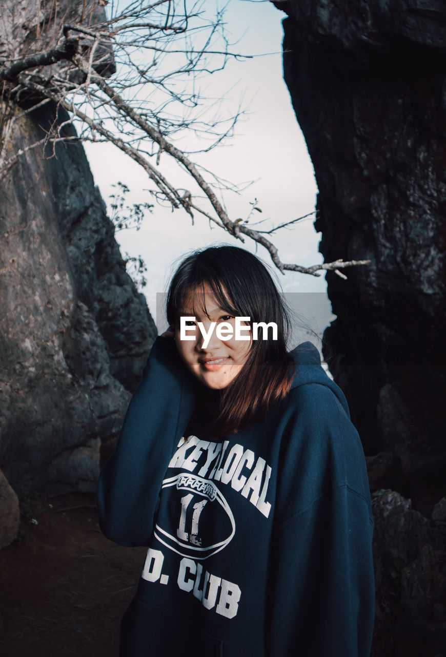 Portrait of smiling young woman standing by tree trunk