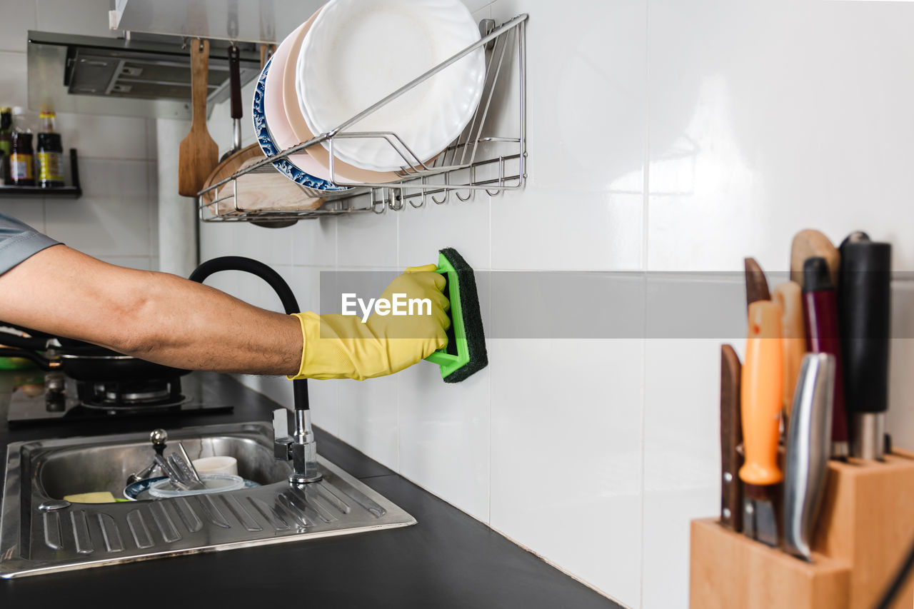  using a plastic brush to scrub the tile wall in the kitchen room.