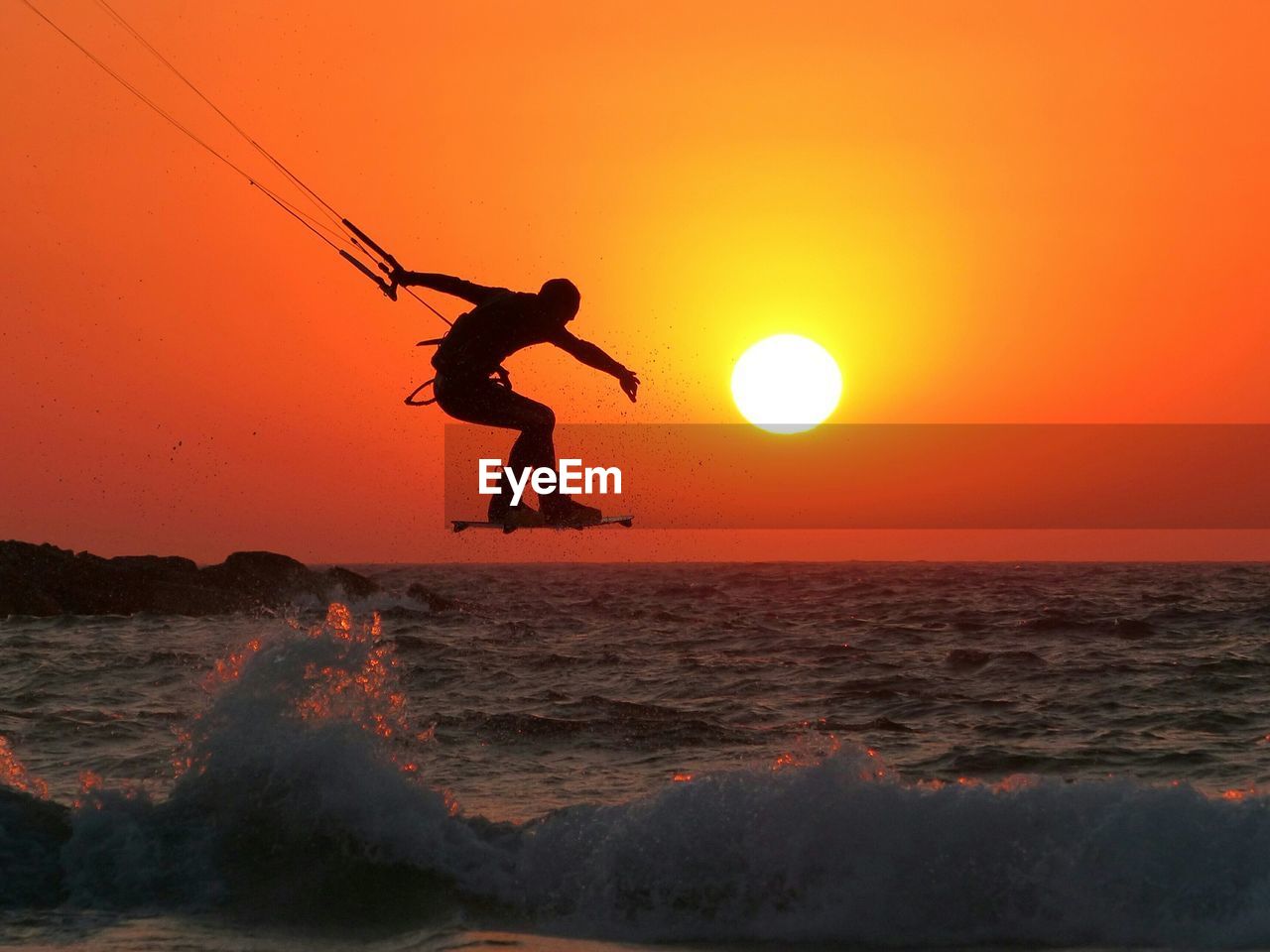 Silhouette man kiteboarding over sea against sky during sunset
