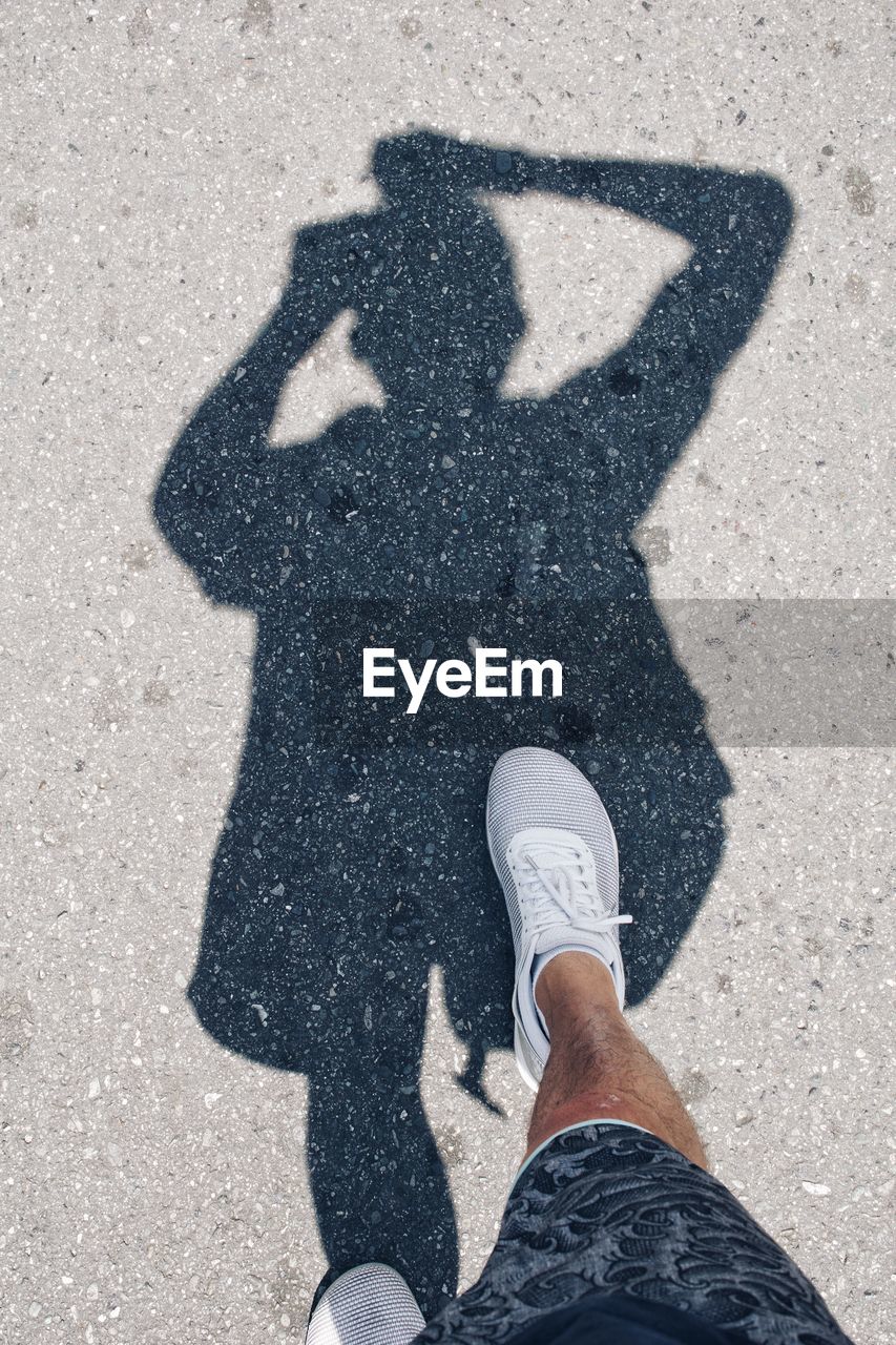 Low section of man walking by shadow on road