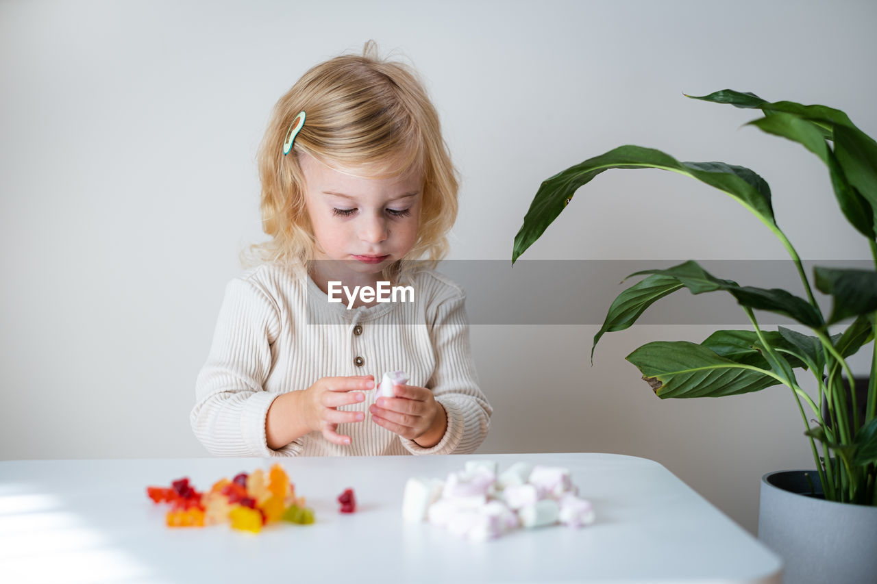 portrait of cute girl sitting on table against wall