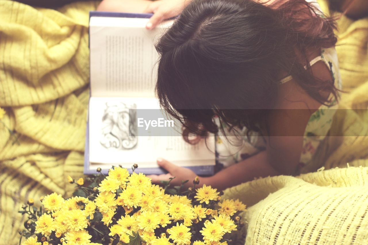 High angle view of girl reading book while sitting on bed at home