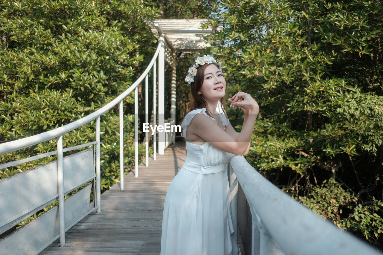 Portrait of bride standing by railing on footbridge in forest