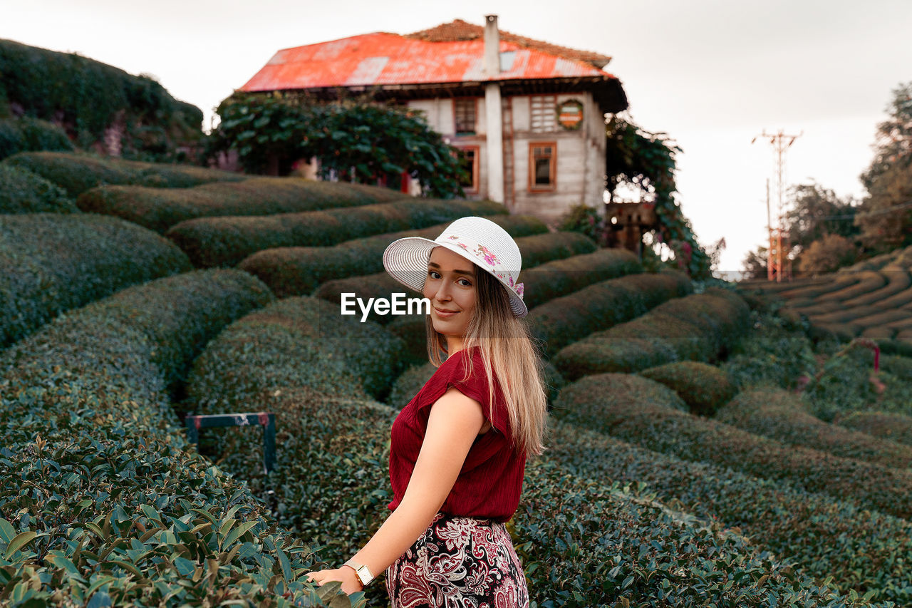 PORTRAIT OF SMILING YOUNG WOMAN STANDING AGAINST BUILDING