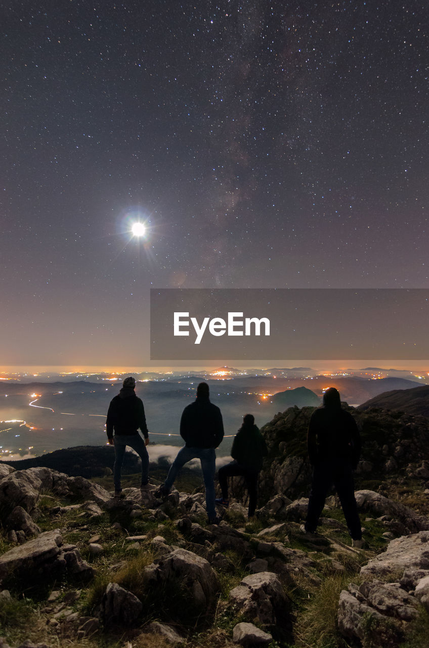 Silhouette people standing on cliff against sky at night