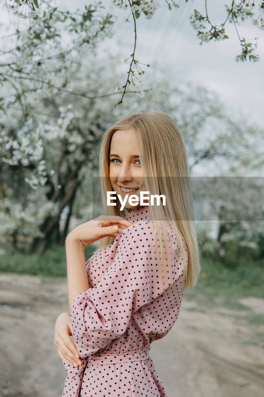 young woman looking away while standing against trees