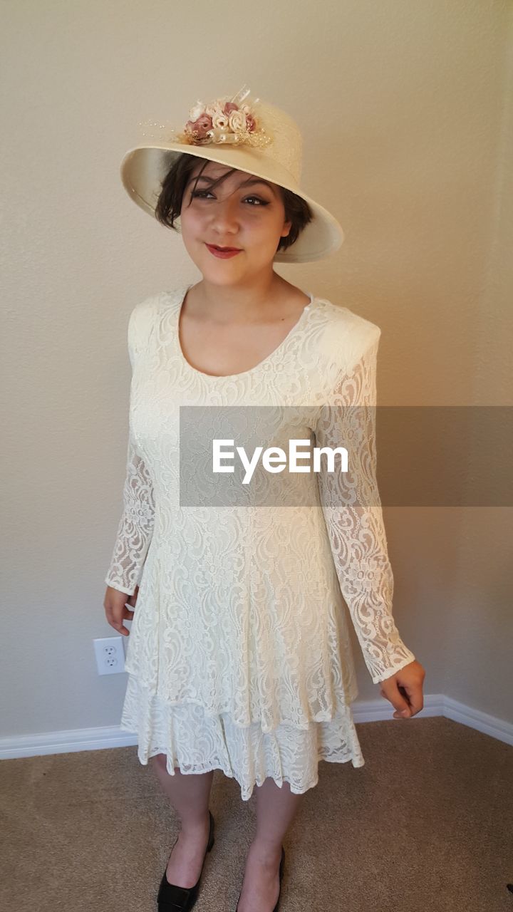 Smiling young woman wearing white dress while standing against wall