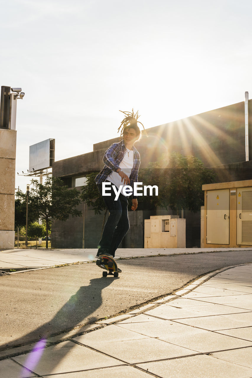 Young man skateboarding on footpath during sunny day