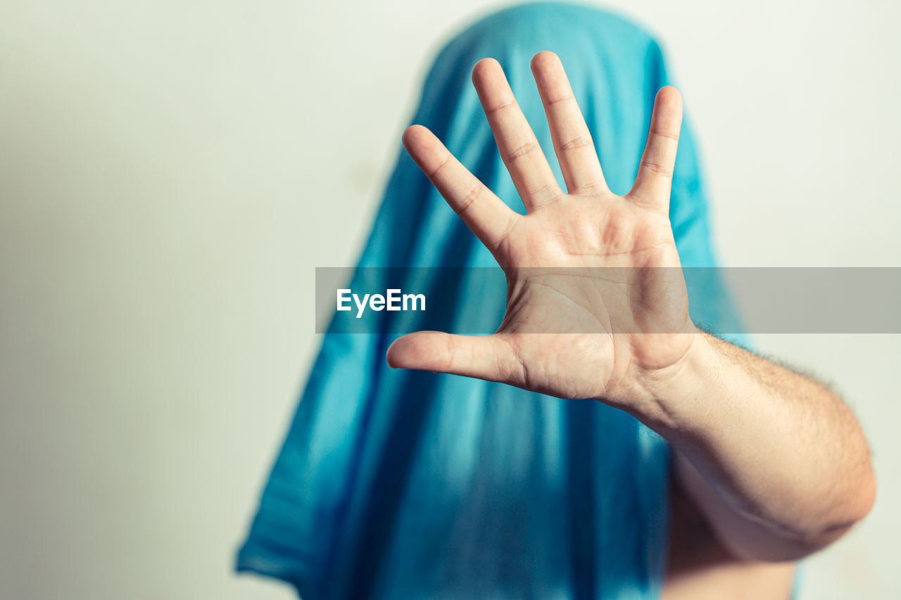 Man hiding the face with a cloth and his hand standing - male hand with stop gesture