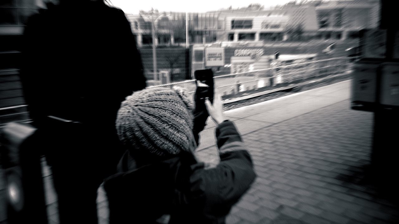 Rear view of boy photographing with smart phone on street