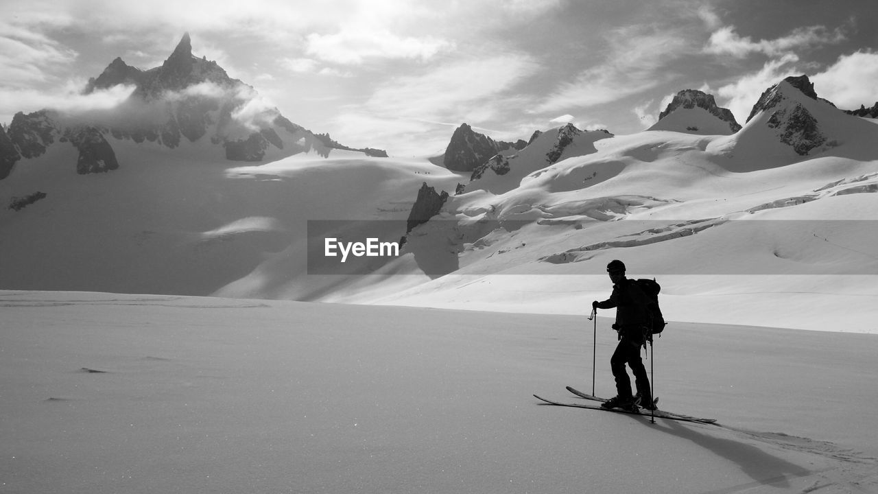 Silhouette skier standing on snowcapped mountain against cloudy sky