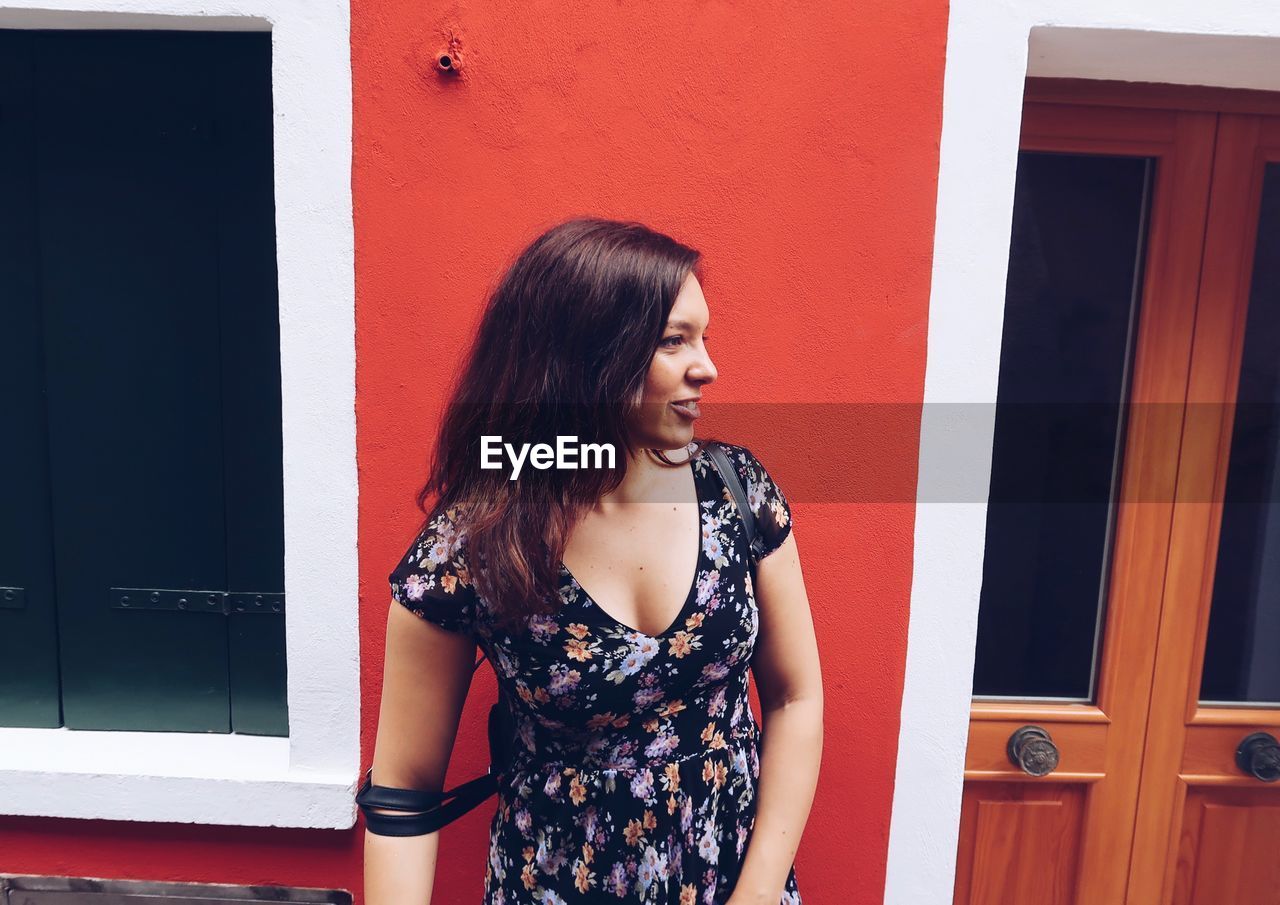 Young woman looking away while standing against wall