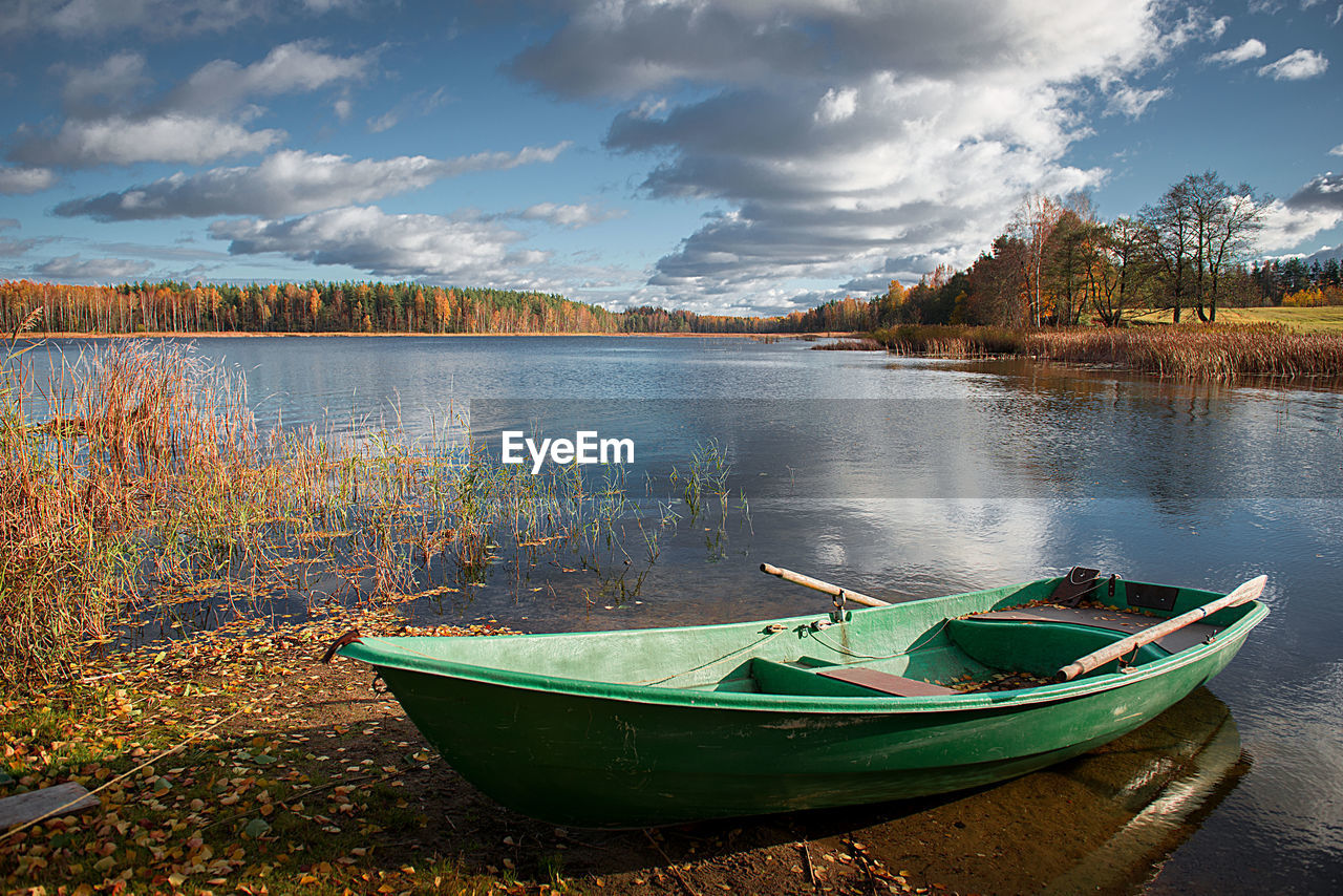 Boat moored on lakeshore against sky during autumn