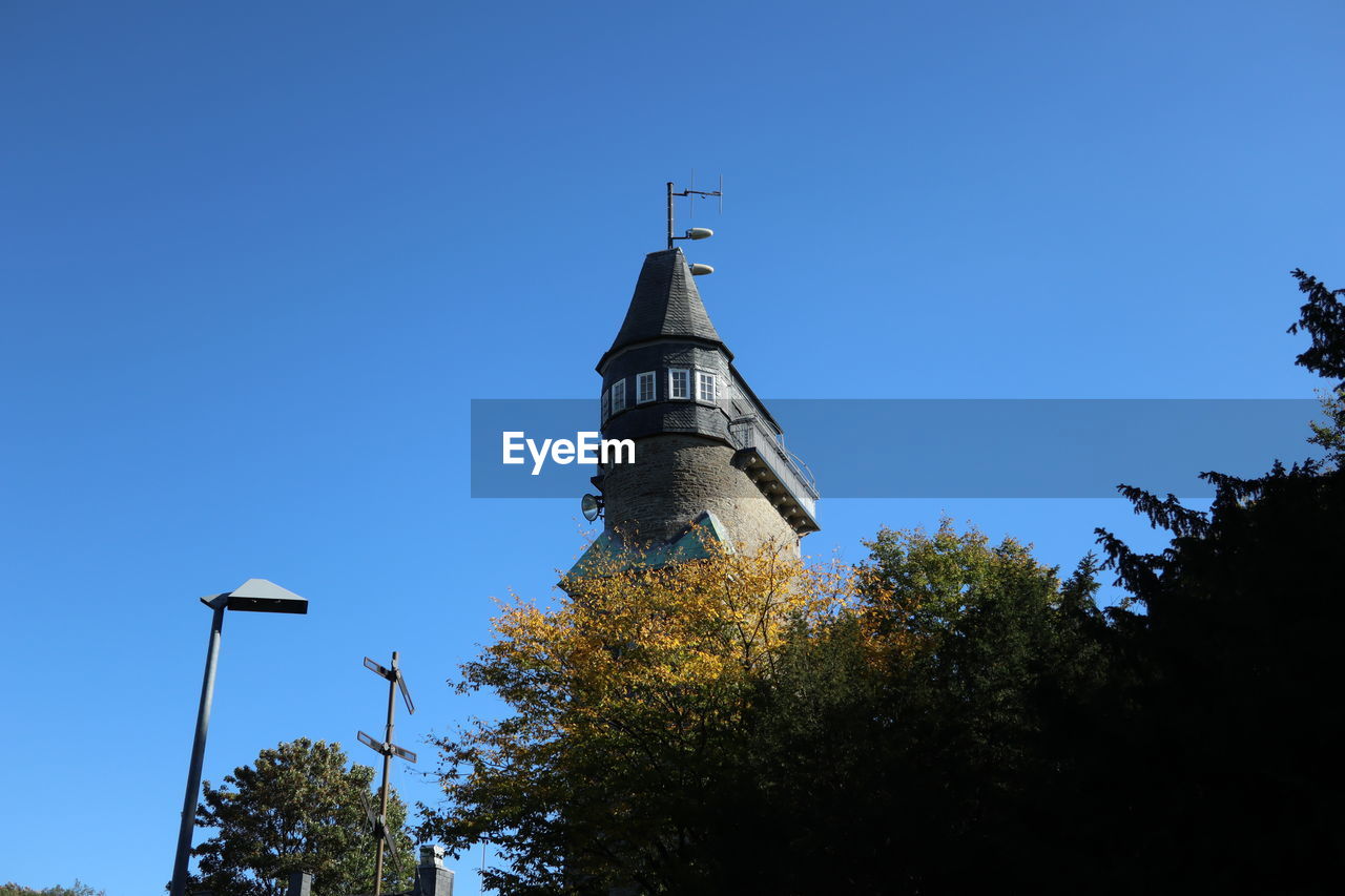 sky, tree, architecture, tower, built structure, plant, clear sky, blue, nature, building exterior, low angle view, no people, steeple, building, travel destinations, history, spire, the past, place of worship, religion, outdoors, sunny, day, landmark, travel, belief, city, street light, copy space, cloud