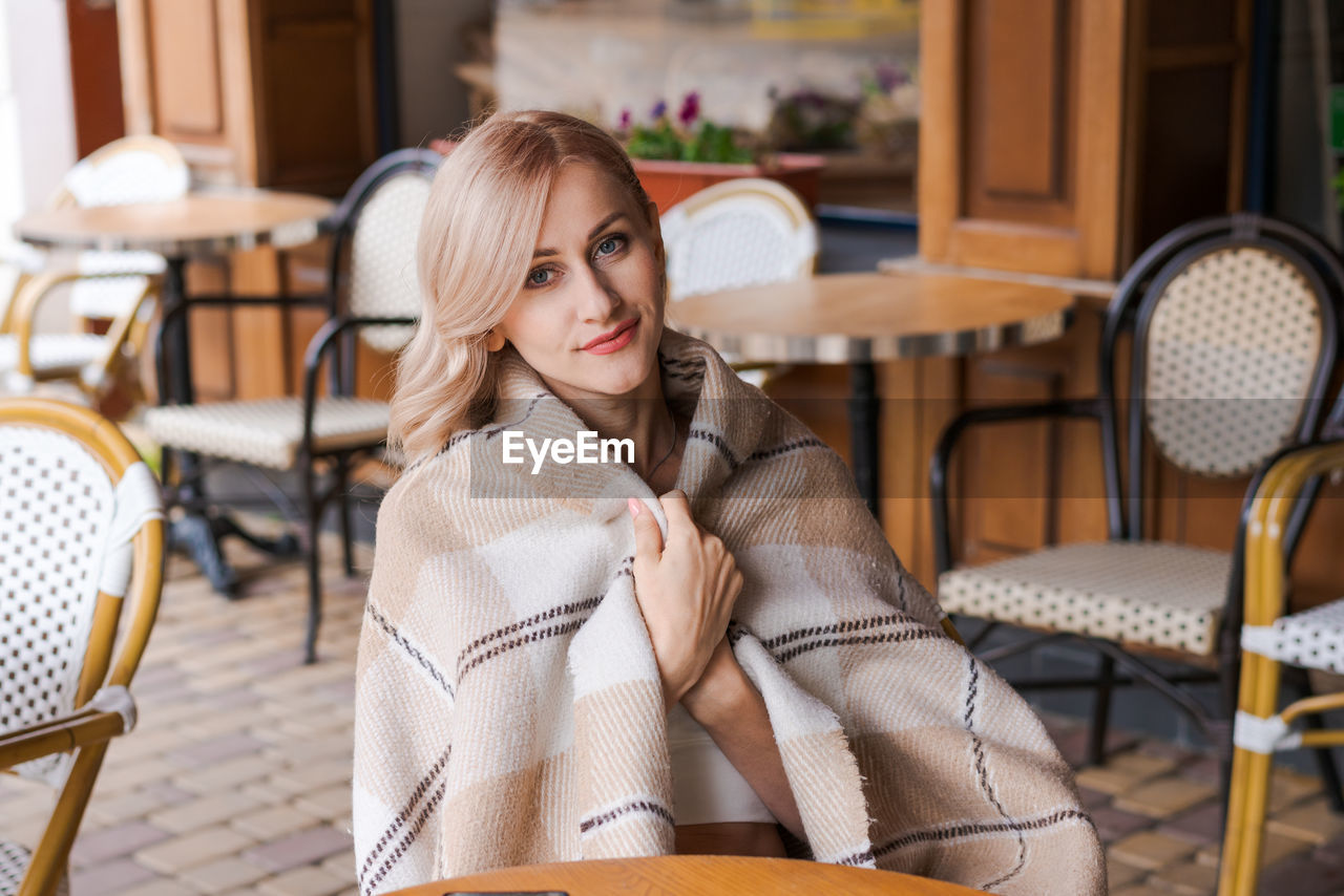 Young beautiful woman, in cafe, drinking coffee in cup, in cozy plaid happy