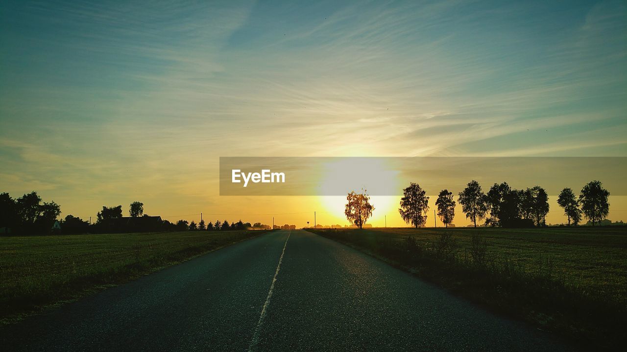 Street amidst field during sunset