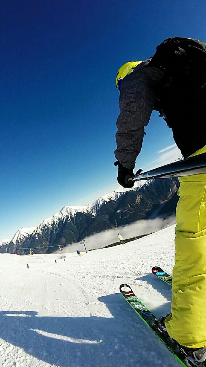 REAR VIEW OF PERSON SKIING ON SNOWCAPPED MOUNTAIN AGAINST CLEAR SKY