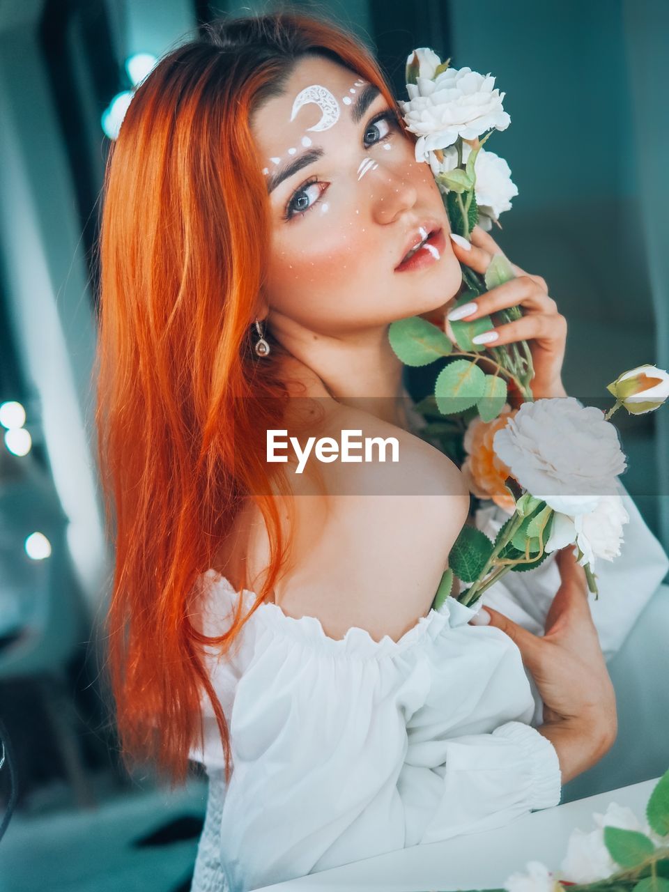 PORTRAIT OF BEAUTIFUL YOUNG WOMAN WITH FLOWER PETALS ON WHITE WALL