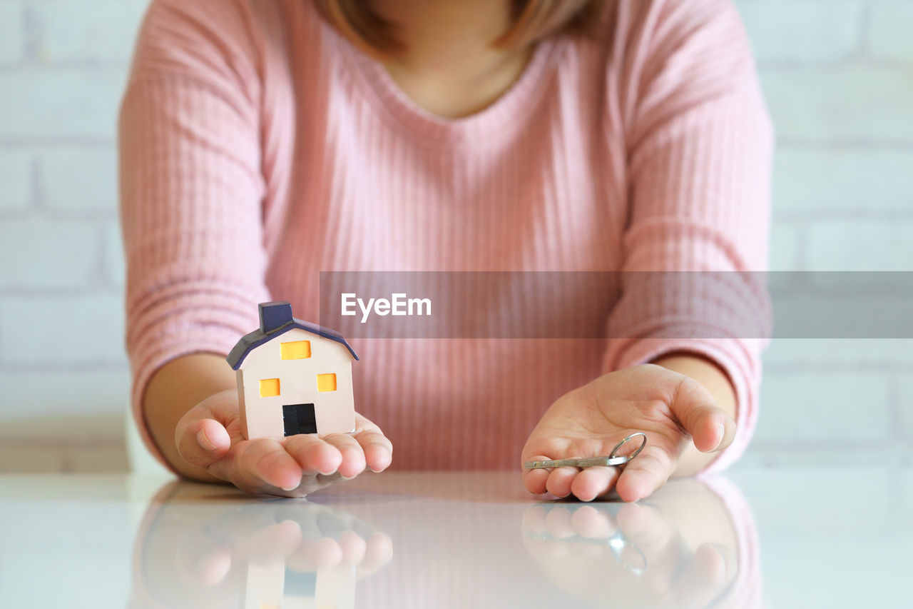 Midsection of woman holding key and model house at table