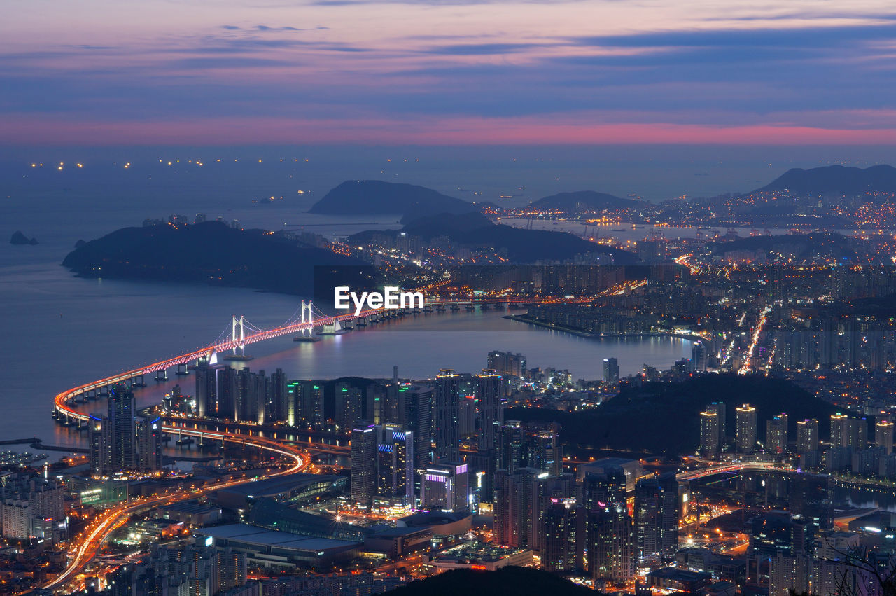 Aerial view of gwangandaegyo over sea by illuminated cityscape during sunset