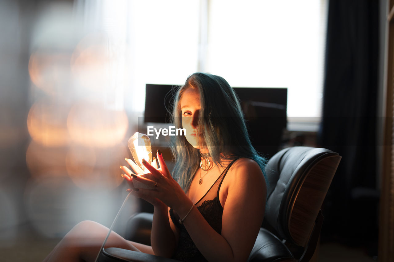 Midsection of woman holding camera while sitting in kitchen