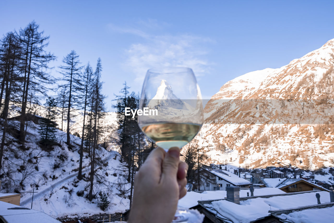 Man holding wineglass viewing matterhorn and snow covered townscape against sky