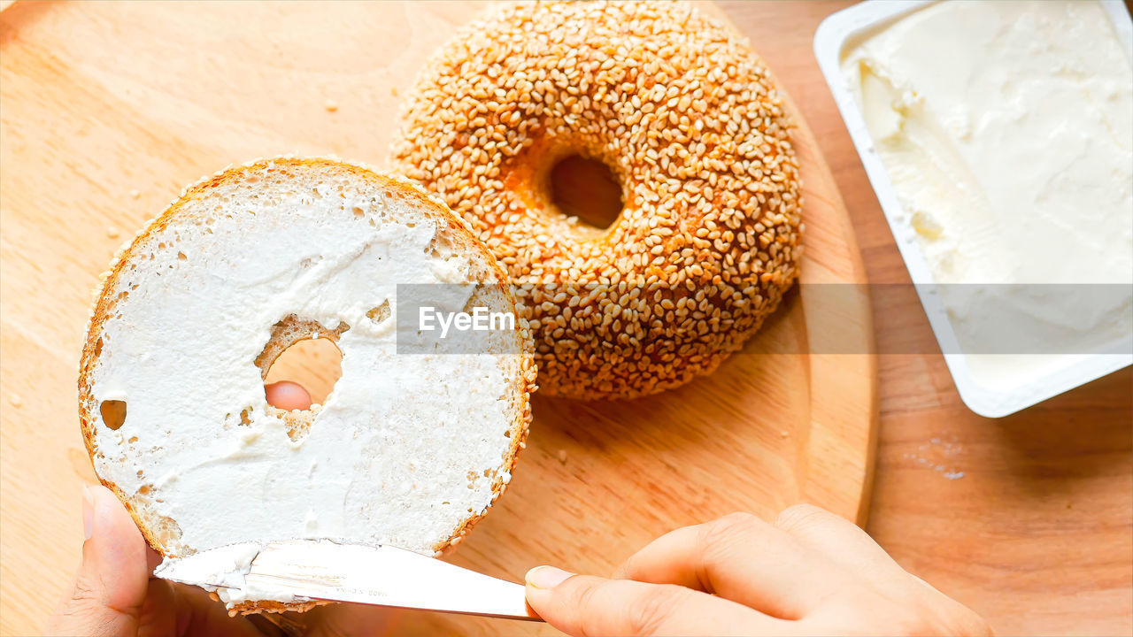 food and drink, food, hand, bagel, freshness, one person, wood, baked, holding, indoors, bread, table, icing, sweet food, high angle view, adult, close-up, lifestyles, healthy eating, cutting board, personal perspective, sweet, women, produce