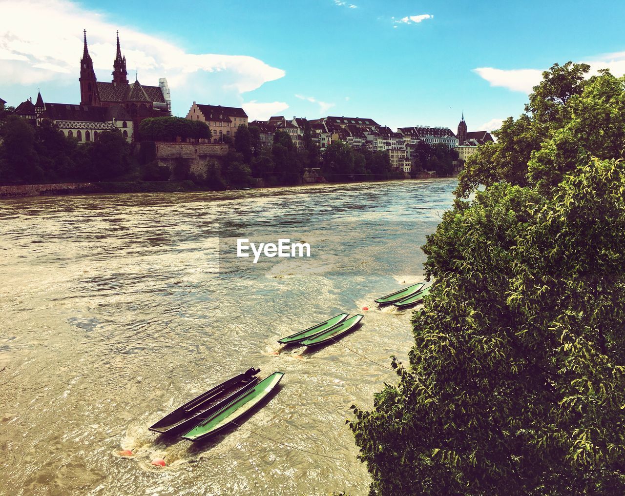 Boats in river by buildings against sky on sunny day