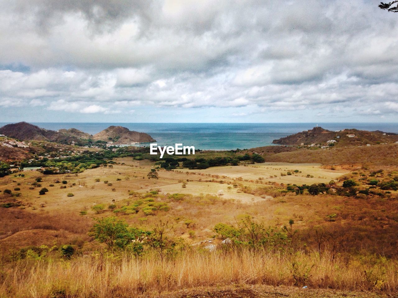 Scenic view of landscape and sea against cloudy sky