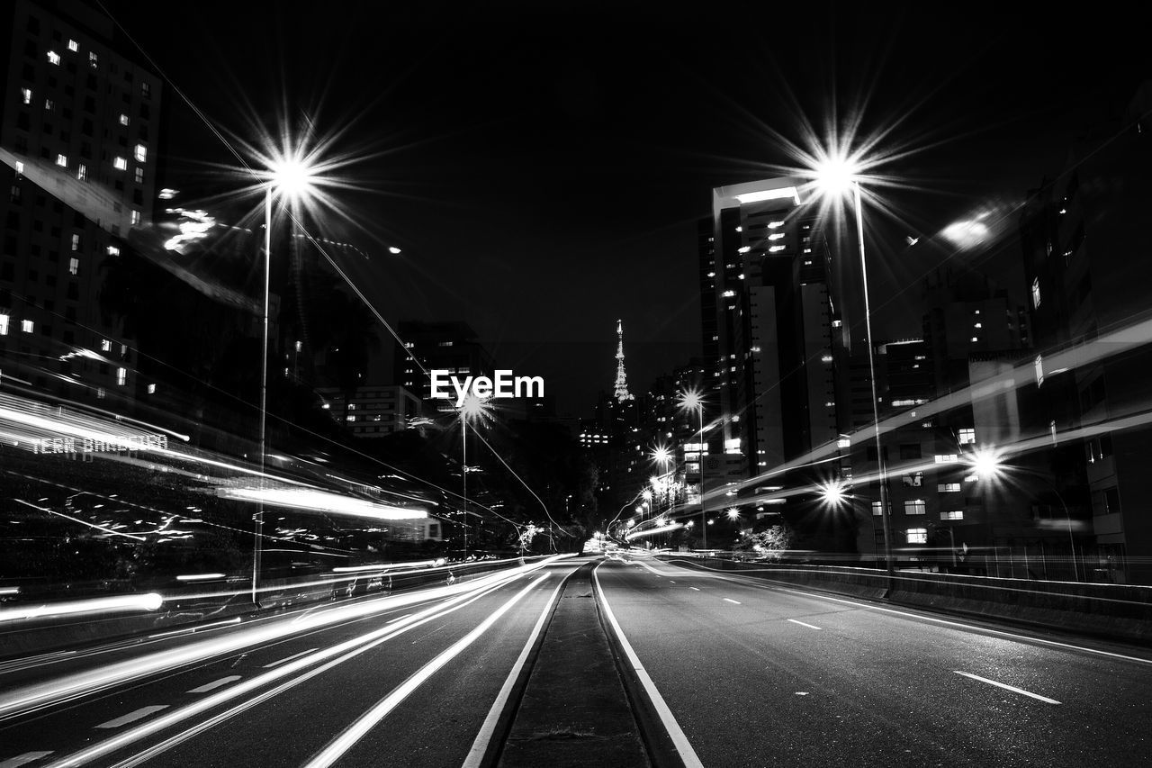 Empty road along illuminated buildings at night