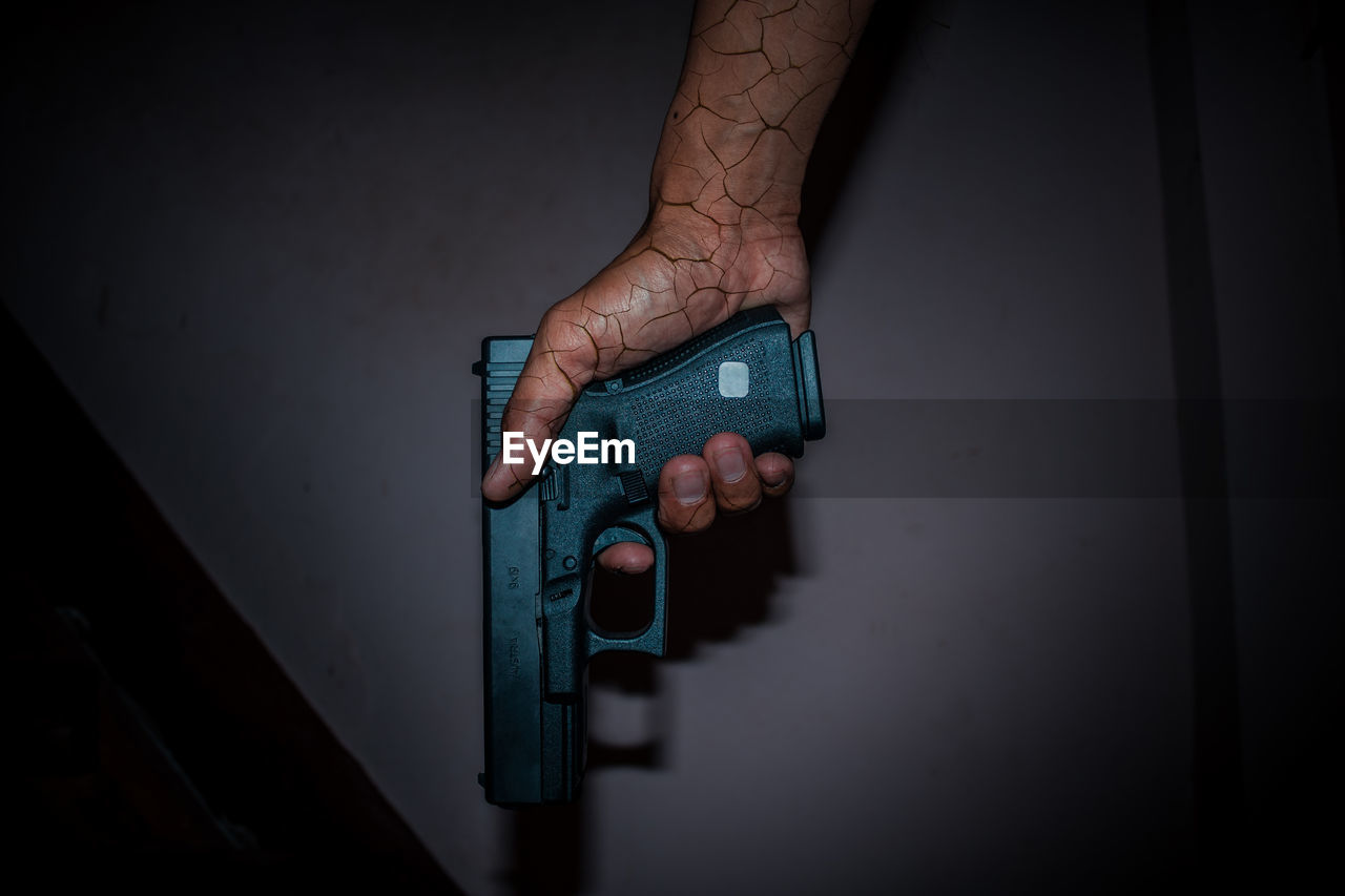 Digital composite image of hand holding gun against wall