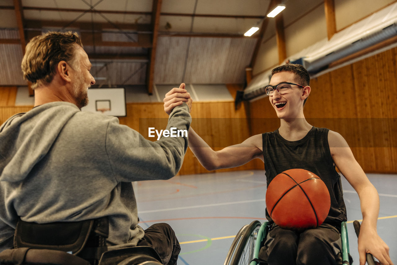 Cheerful male and female athletes with disabilities doing handshake while playing basketball at sports court
