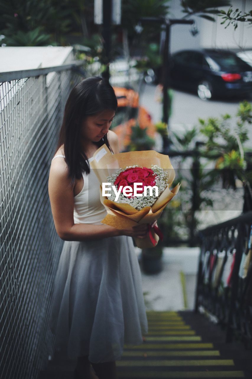 High angle view of young woman holding bouquet while standing on stairs