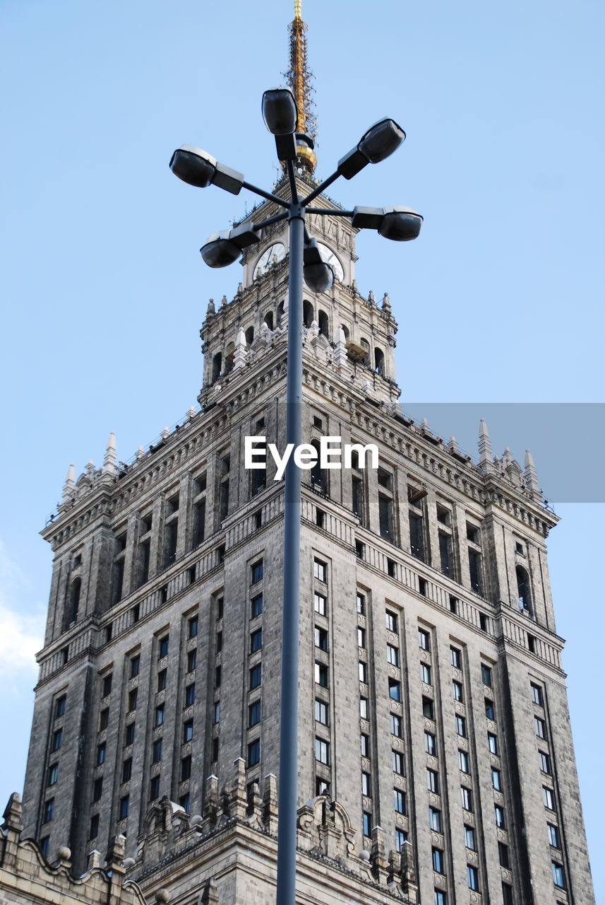 Low angle view of street light and palace of culture and science against clear sky