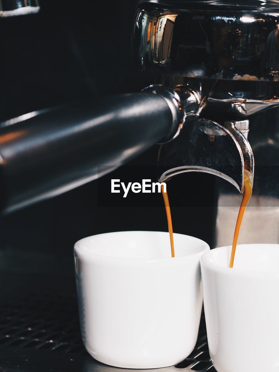 Close-up of machinery pouring coffee in cups at cafe