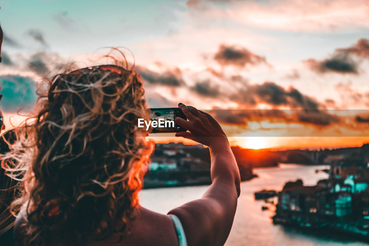 Midsection of woman photographing sea against sky during sunset