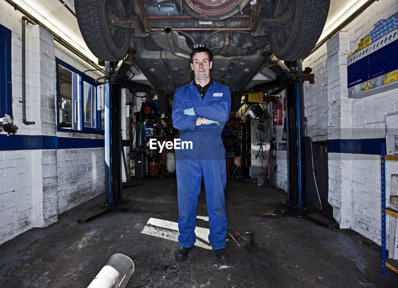 Car mechanic posing under a car at automotive garage in the uk