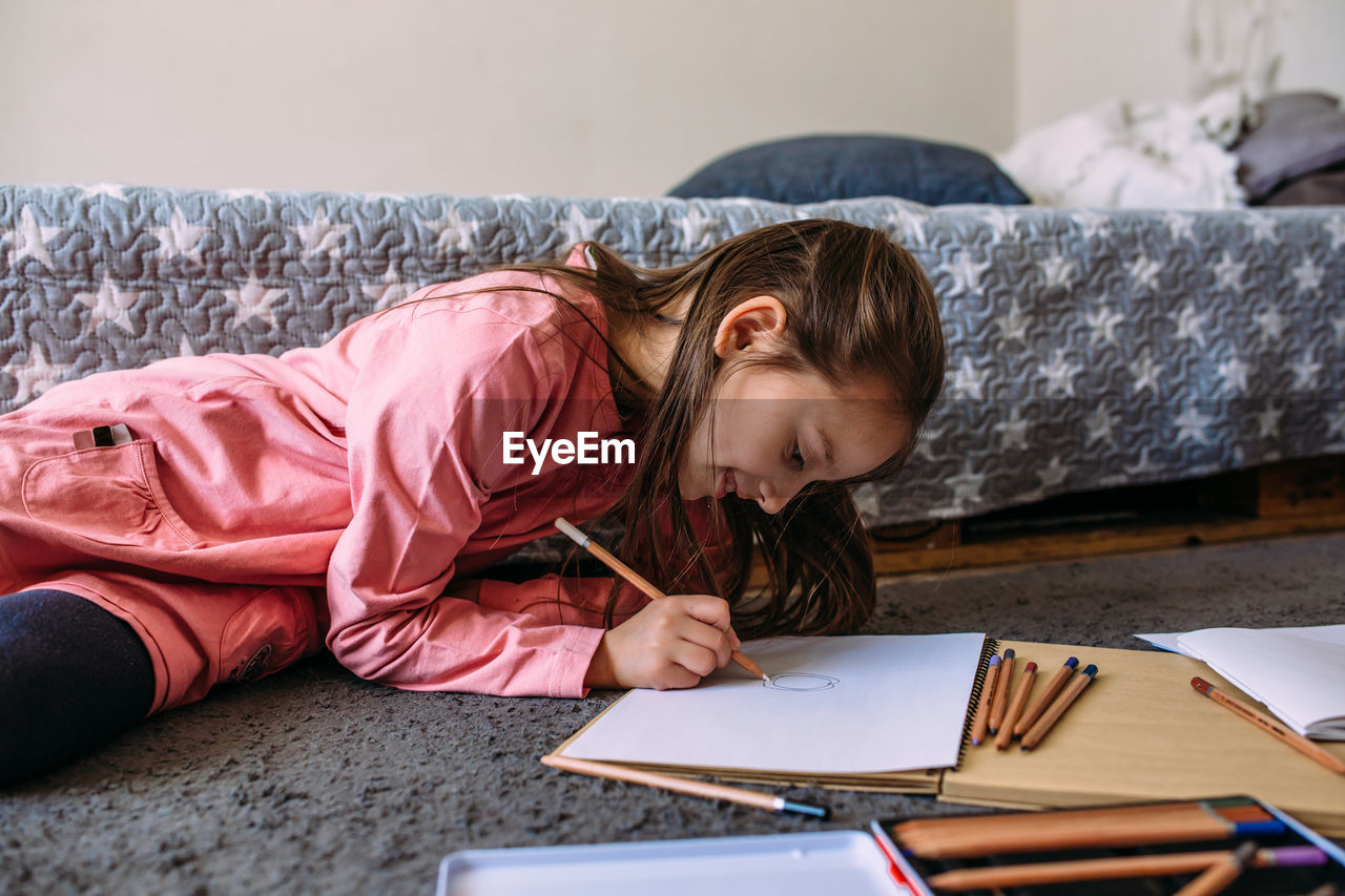 The girl after school plays at home, draws with pencils and felt-tip pens