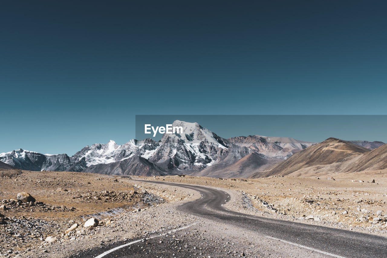 Road leading towards mountains against clear blue sky